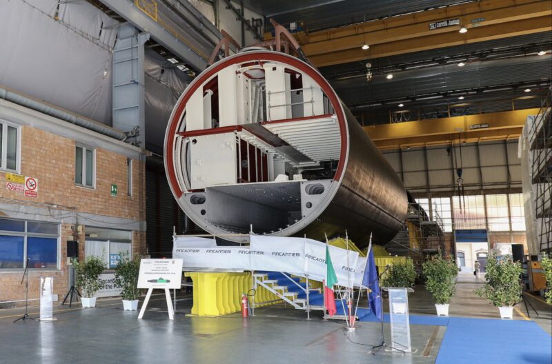 Hull section of the second U212NFS submarine on yellow supports at Fincantieri's Muggiano shipyard, with Italian and EU flags for the keel-laying ceremony